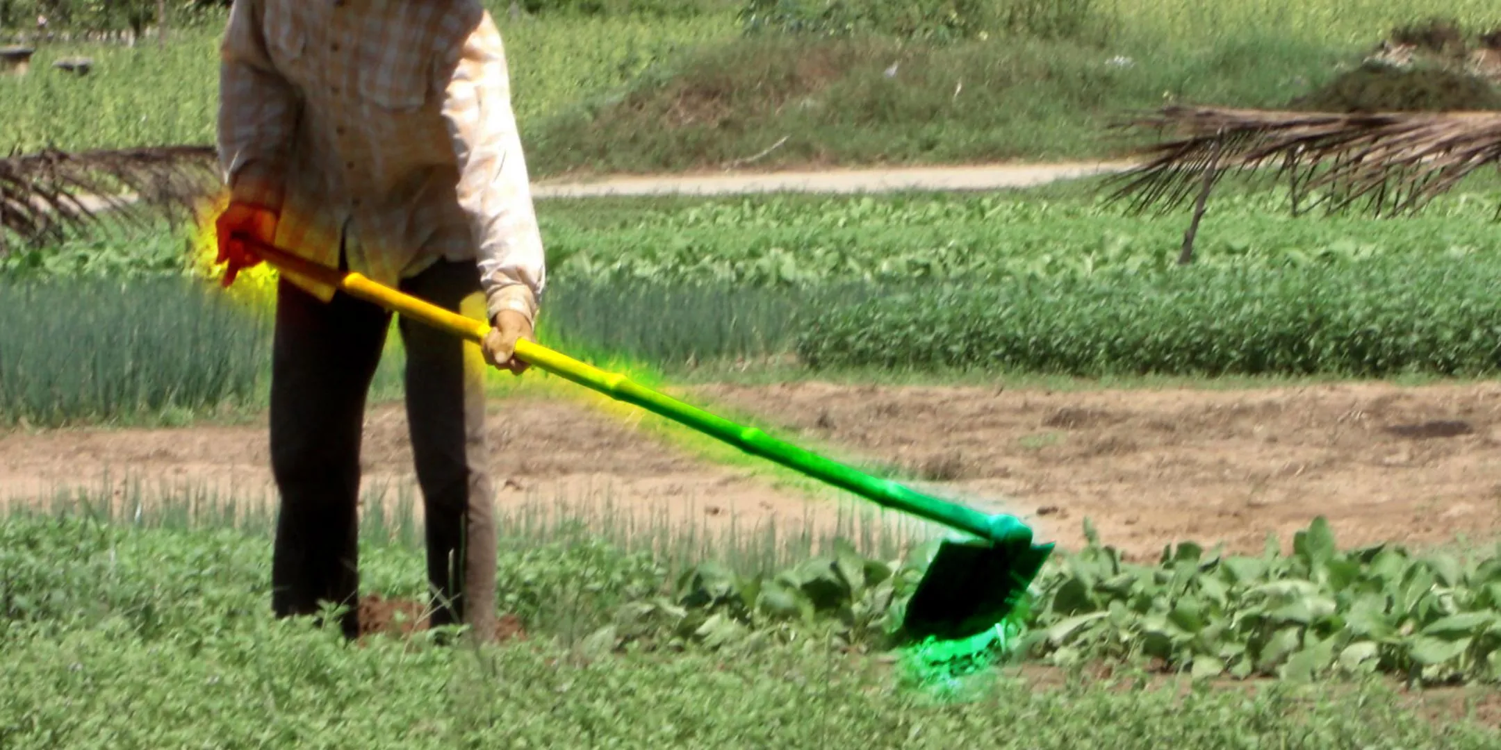 Một nông dân đang sử dụng cái cuốc trên cánh đồng, nhưng cái cuốc phát sáng nhiều màu sắc như cầu vồng, minh họa cho ý tưởng công cụ nông nghiệp 'gamer' với đèn LED.